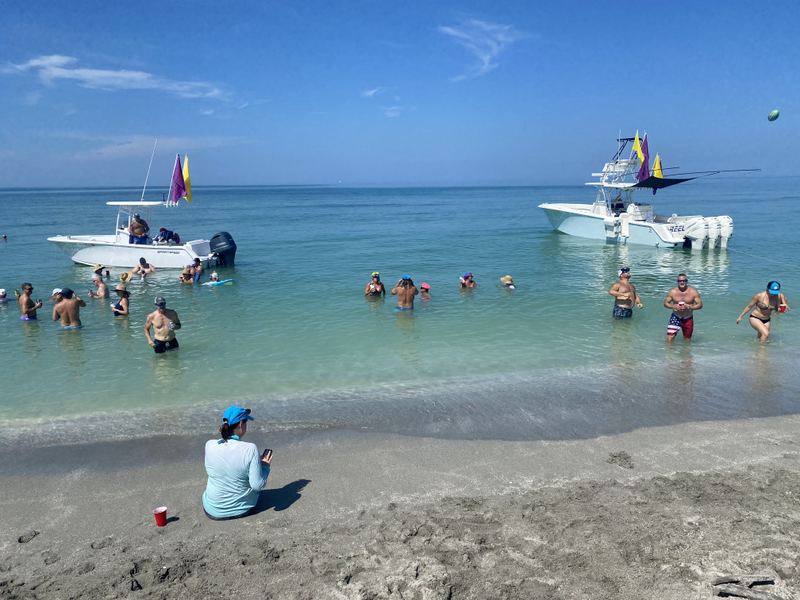 Boats rafted up at a Sarasota sandbar with beachgoers wading, a stop on the tiki-bar crawl