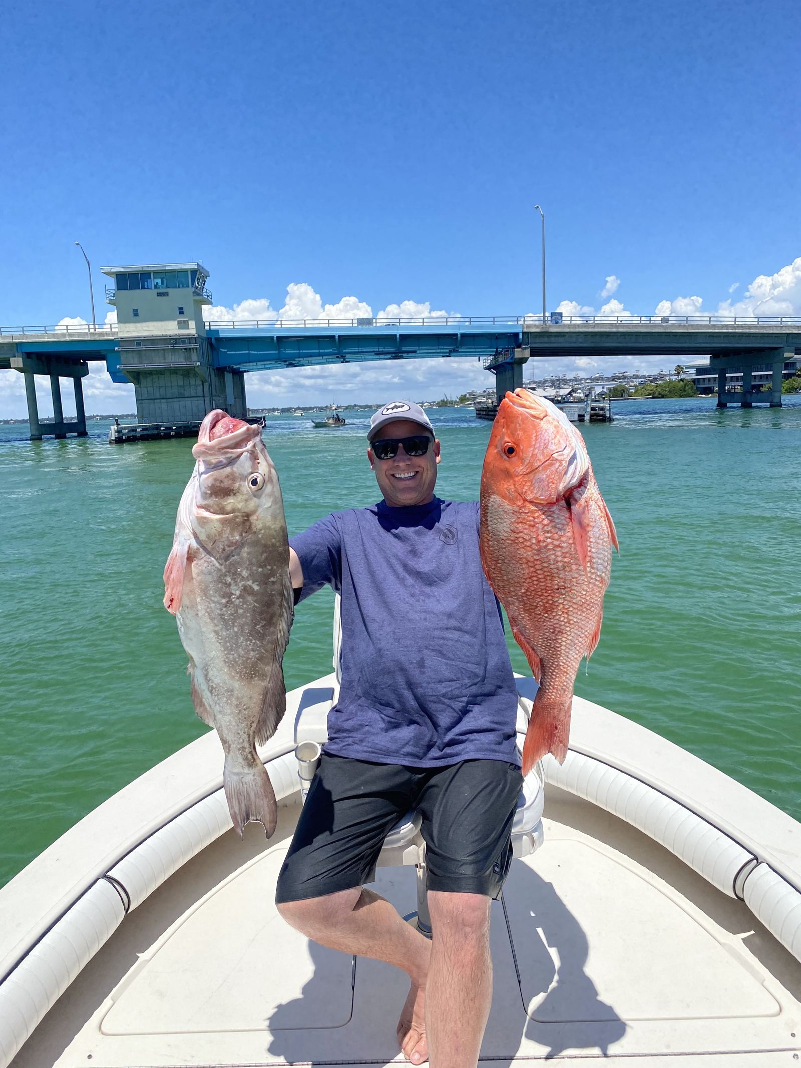 An angler holding a gag grouper in one hand and a red snapper in the other on the bow of a center console