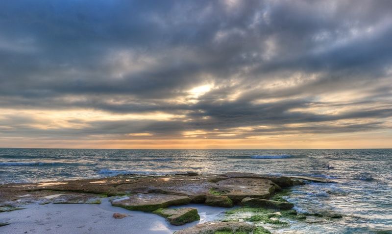 Flat limestone ledges running out of the sand into breaking surf under a heavy sunset sky
