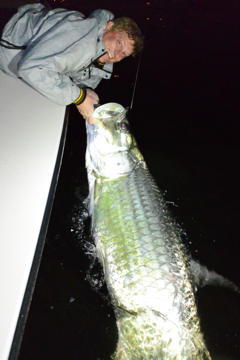 Angler in a rain jacket holding a big silver tarpon boat-side at night on a Sarasota charter